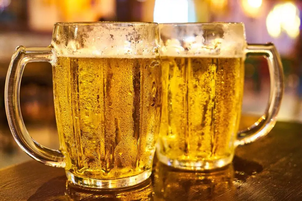 Two clear glasses filled with cold beers were placed on a brown wooden table at a bar
