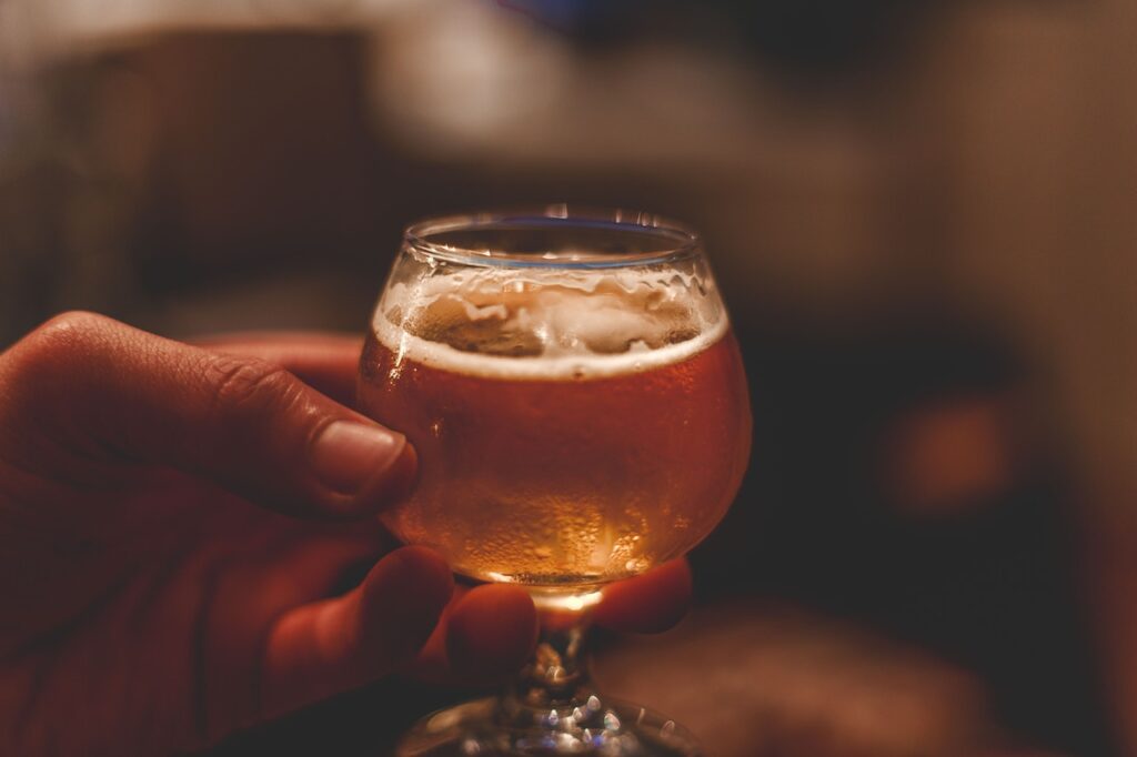 A person holds a wine glass filled with a cold beer at a beer shop