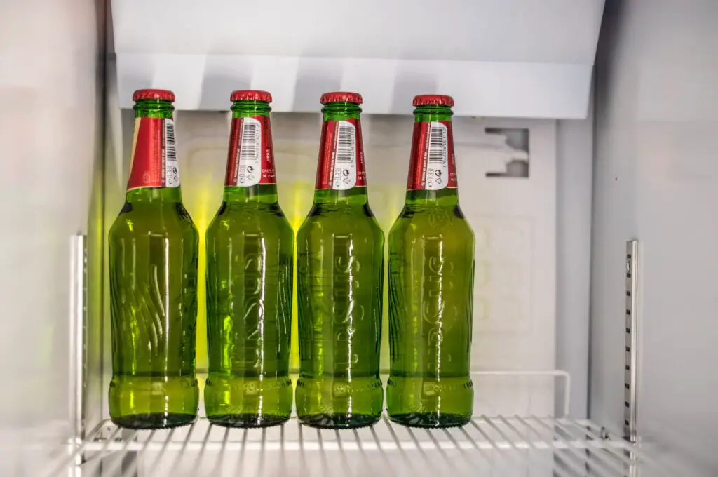 Four green bottles of Ursus beer stored vertically in an open white fridge