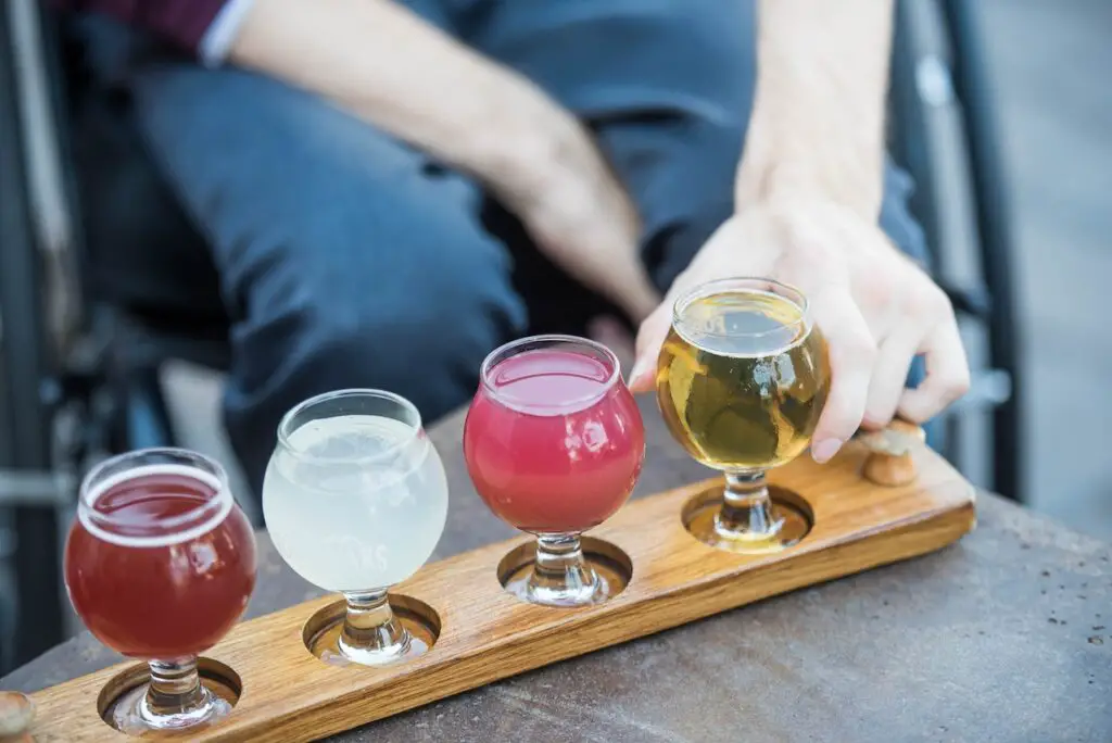 Four different kinds of alcoholic beverages are in wine glasses placed on a brown wooden rack on a table