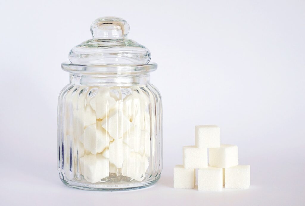 A clear glass jar filled with cubes of white sugar was placed on a white surface