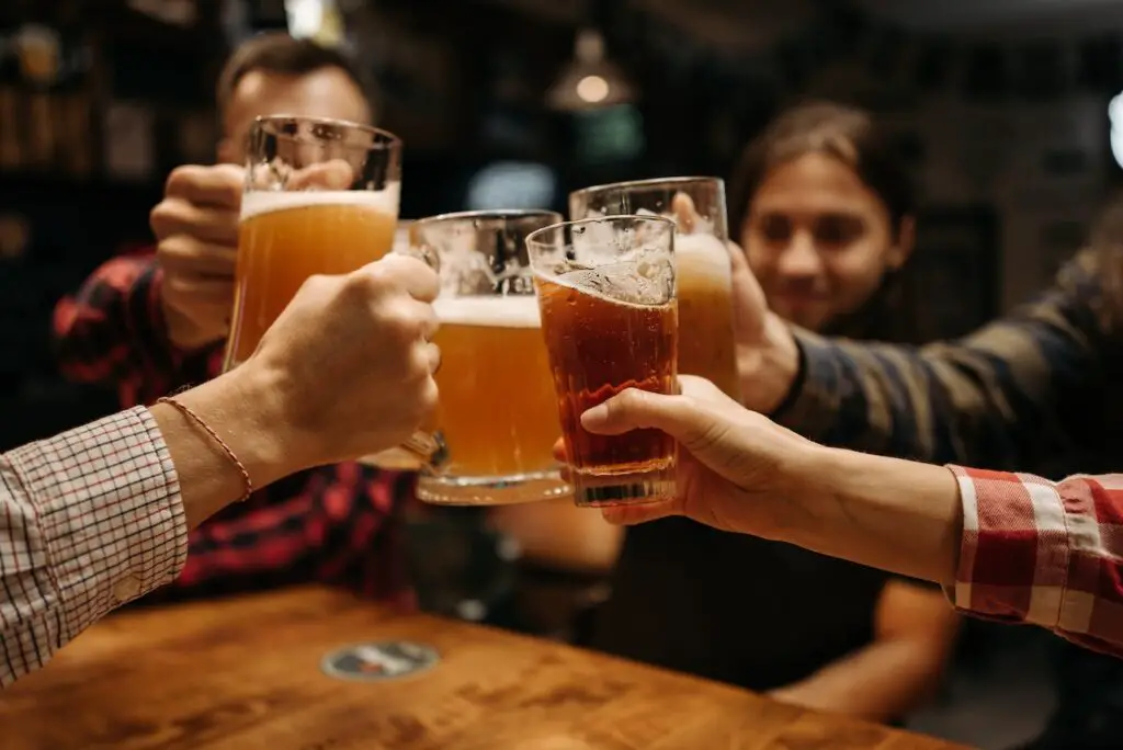 A group of people raising their cold beer in a clear glass near a brown wooden table in a pub