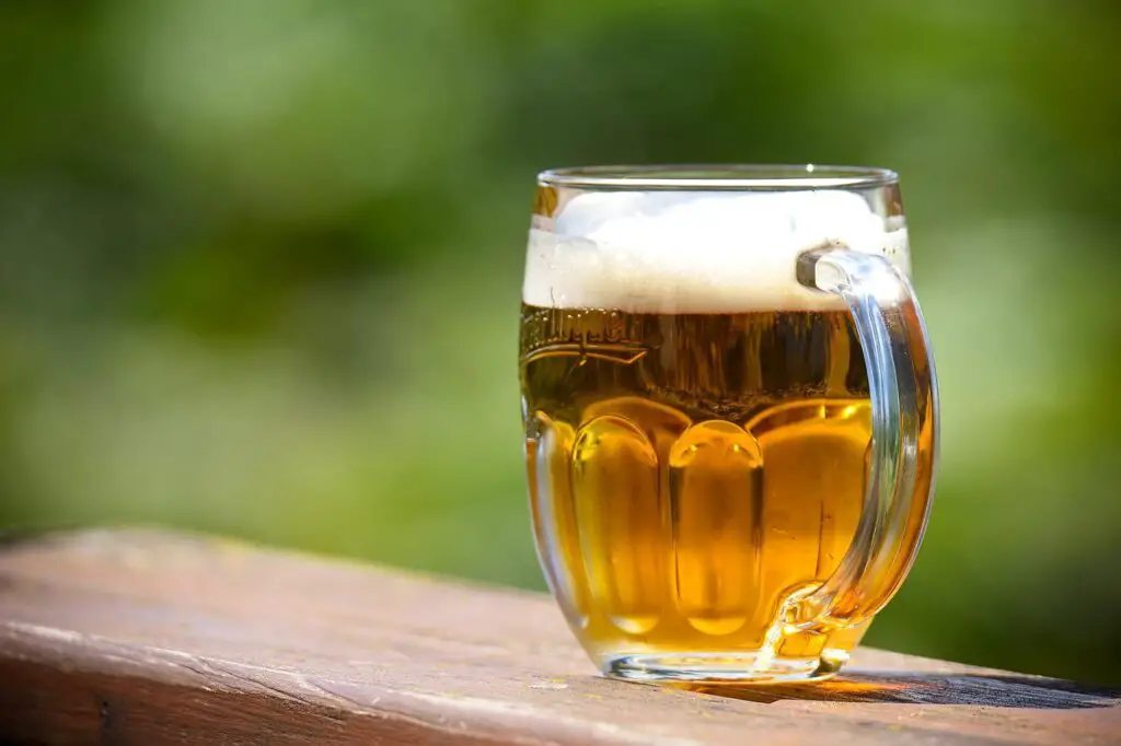 A clear mug filled with beer was placed in a brown wooden chair outside the house