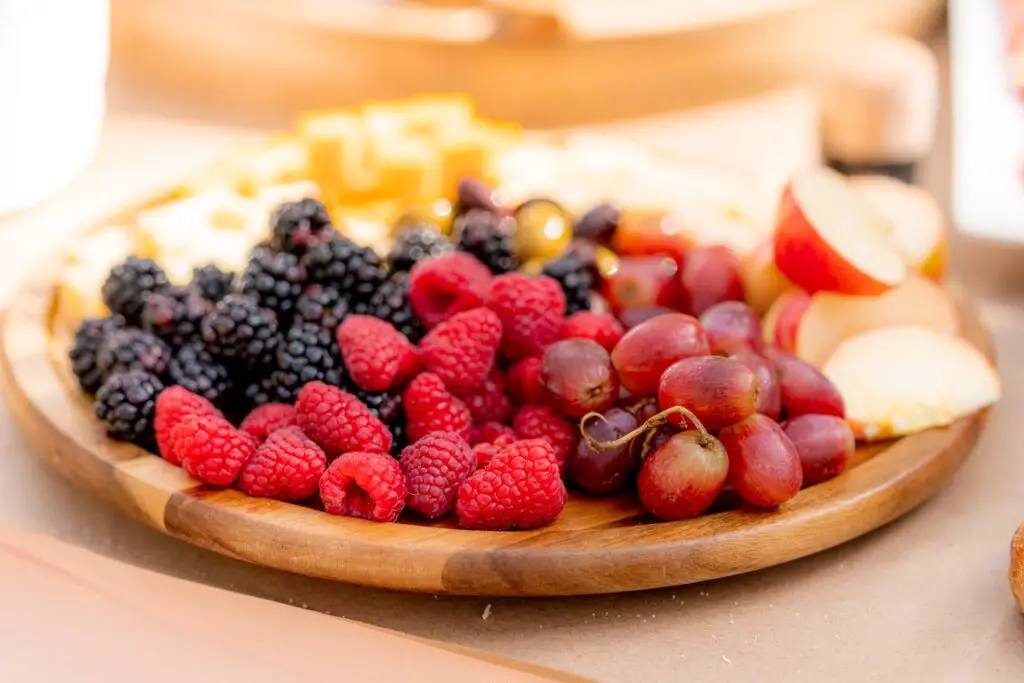 Different types of fresh fruits are placed on a brown wooden plate on top of a white surface