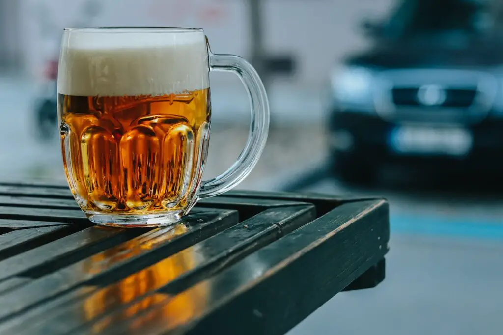 A clear mug filled with foamy beer was placed on top of a green wooden table outside the bar