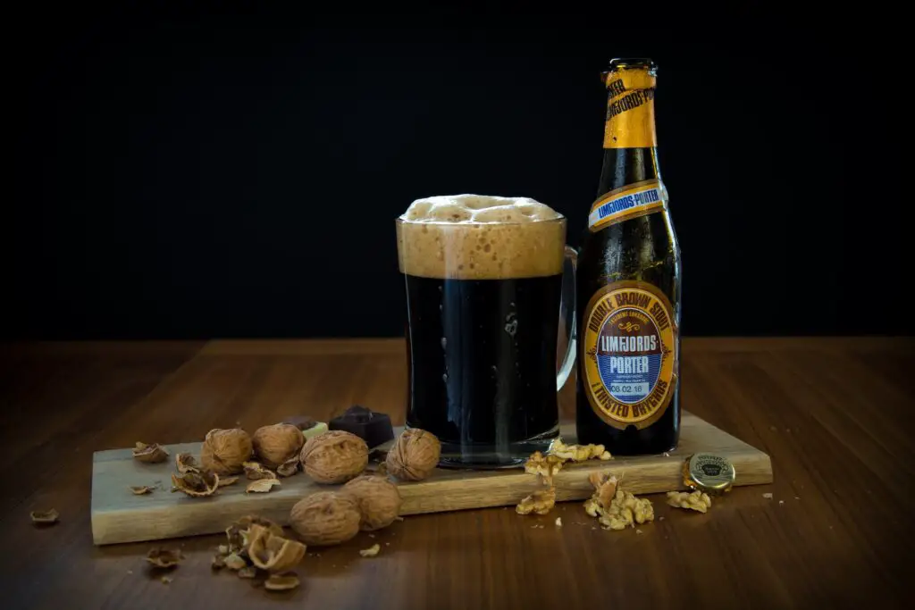 A bottle of Limfjords Porter double brown stout beside a mug filled with beer and peanuts on top of a brown wooden piece