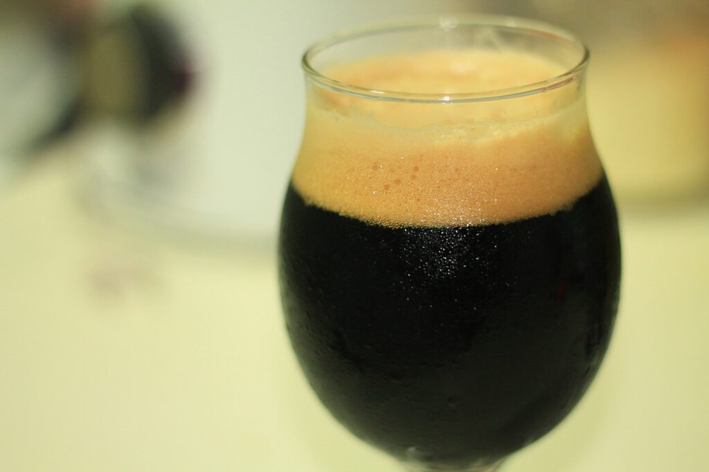 A cold dark frothy Baden stout in a clear glass on a white surface