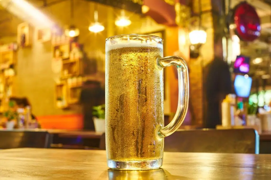 A clear mug filled with a cold beer was placed on a brown wooden table in the bar