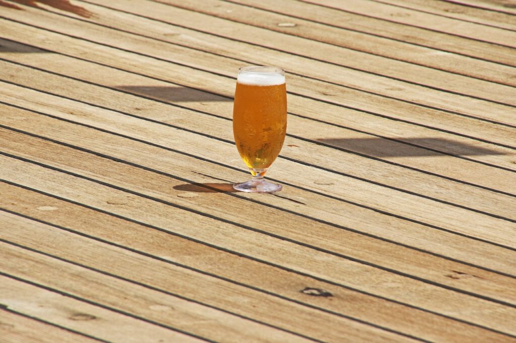 A clear short-stem wine glass filled with beer was placed on a brown parquet flooring outside the house
