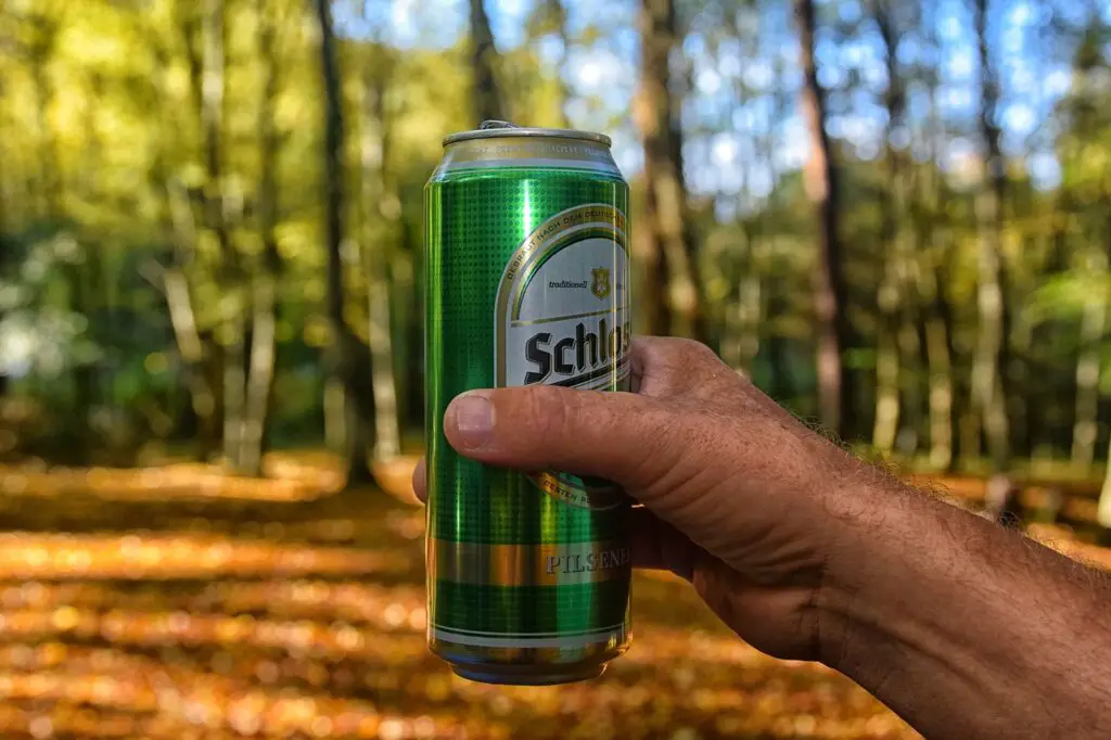 A person holding a can of beer while in the middle of the forest