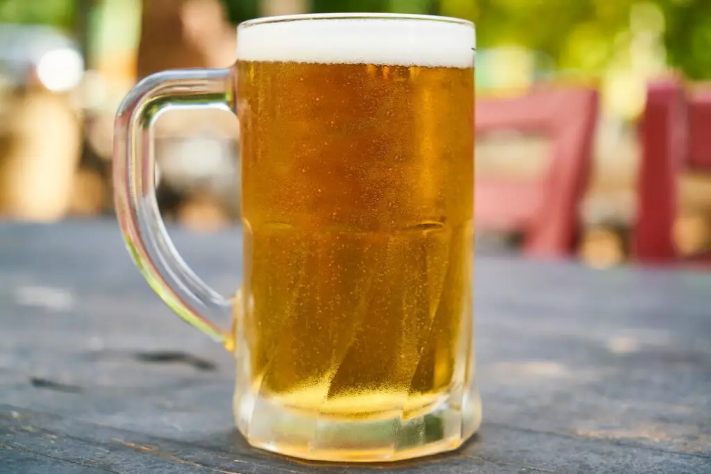 A clear glass of beer filled cold beer on top of a brown wooden table