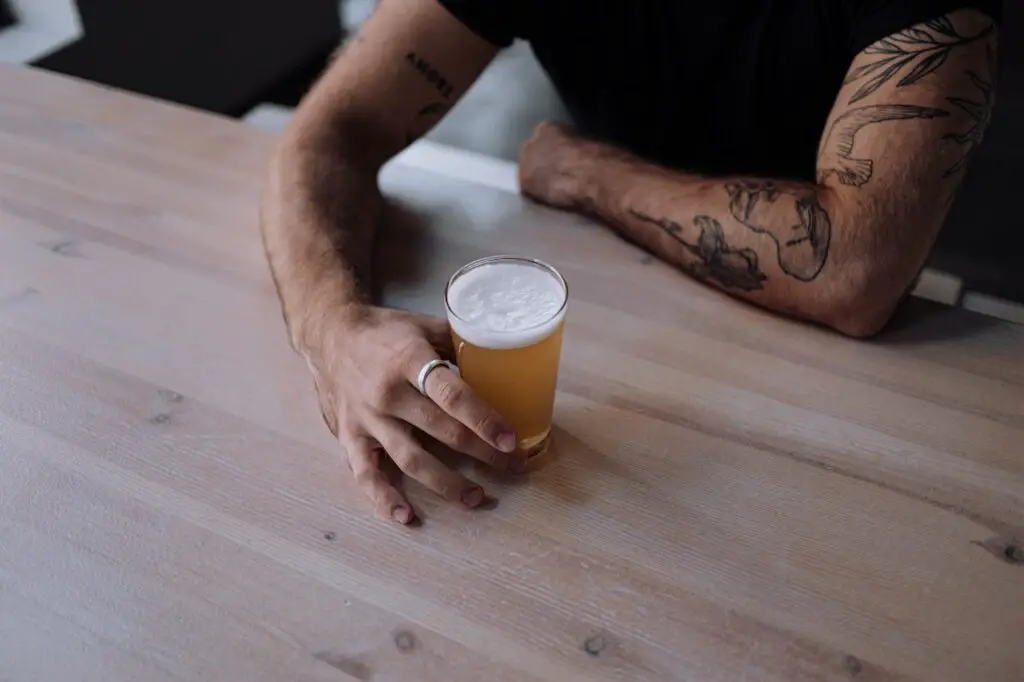 A person wearing a black shirt and silver ring is holding a glass of beer on top of a wooden table