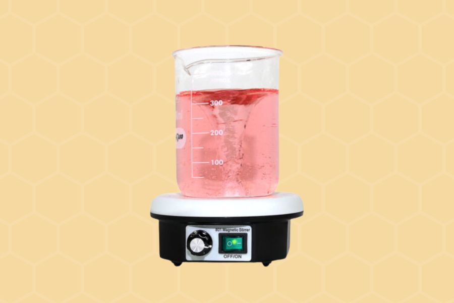 A clear beaker filled with pink liquid on top of a black and white stir plate