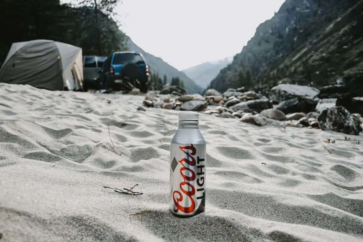 A can of Coors light beer placed on the white sand of a camping site
