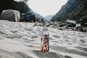 A can of Coors light beer placed on the white sand of a camping site