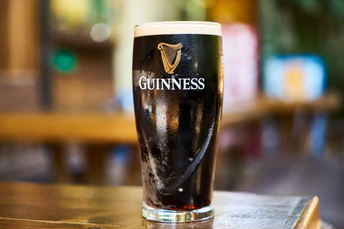 A clear glass filled with Guinness beer was placed on a brown wooden table
