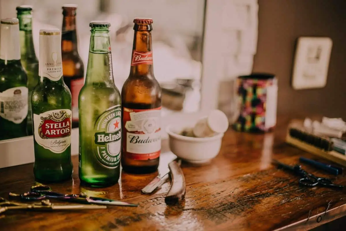 Three assorted beer beverages beside different scissors placed on a brown wooden table
