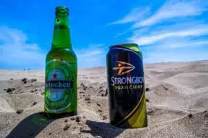 A bottle of Heineken and a can of Pear Cider were placed on a sand